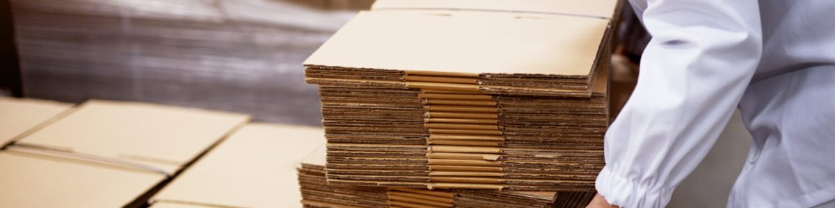 Close up of young female worker picking up stacks of folded cardboard boxes from a bigger stack in factory storage room. manufacturing employee stacks of folded cardboard boxes