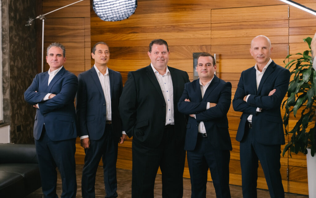 Group photo of Exigy’s leadership team standing together in formal business attire inside a modern office.